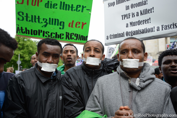 Men demonstrate with bound hands and taped up mouths in protest.