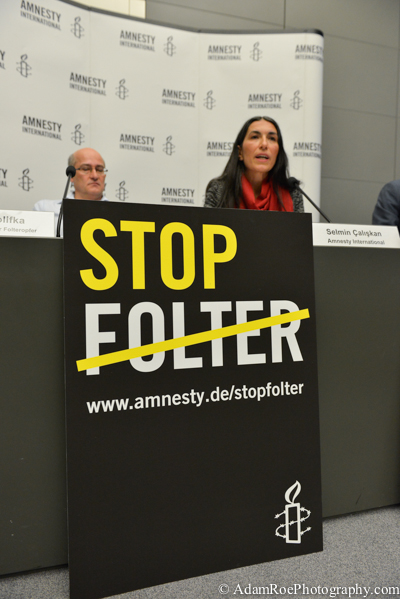 Matthias Polifka and Selmin Caliskan at the press conference, behind a sign that reads "Stop Torture".
